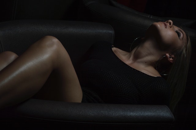 Žena v čiernom tričku s holými nohami leží na čiernom gauči